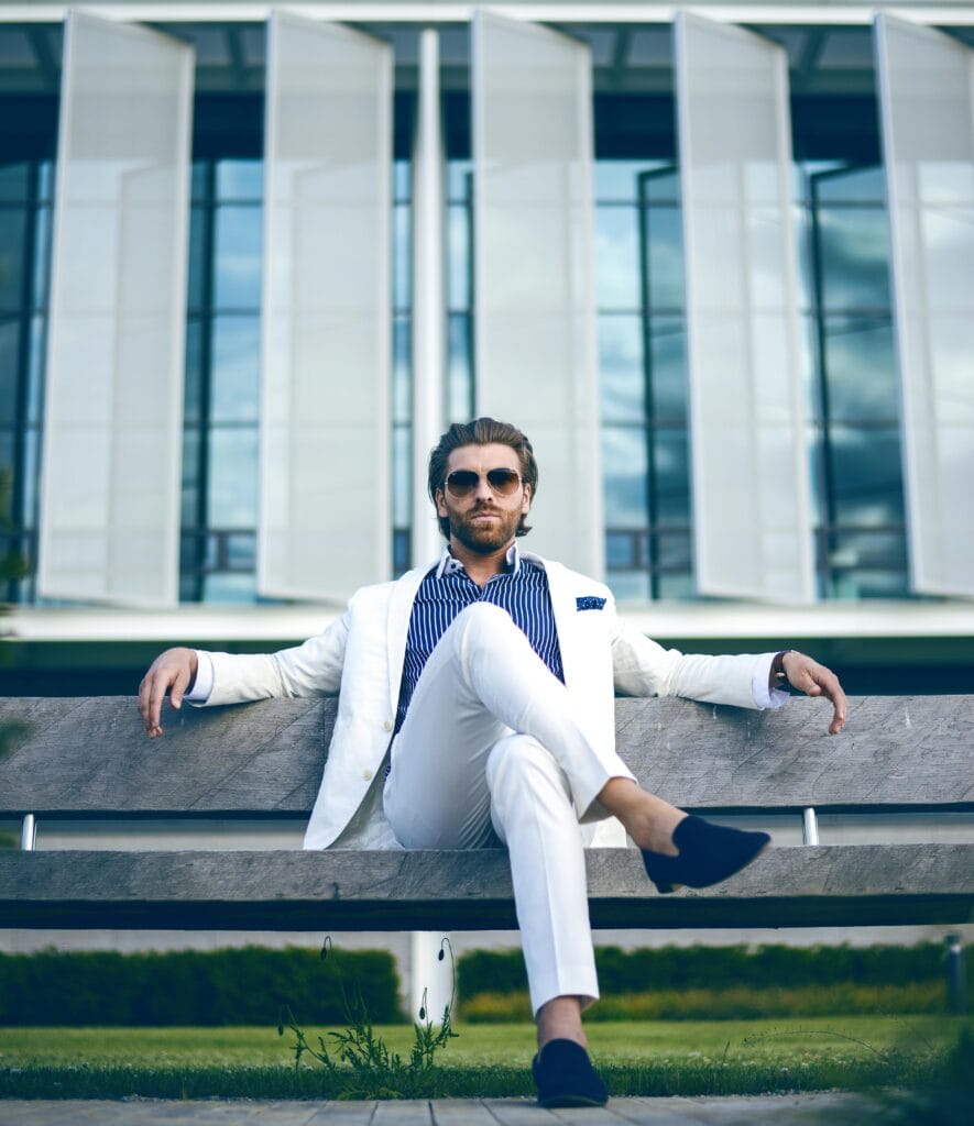 pexels-photo-2709563-2709563 Fashionable man in white suit sitting confidently on a bench outdoors, embodying elegance and modern lifestyle.